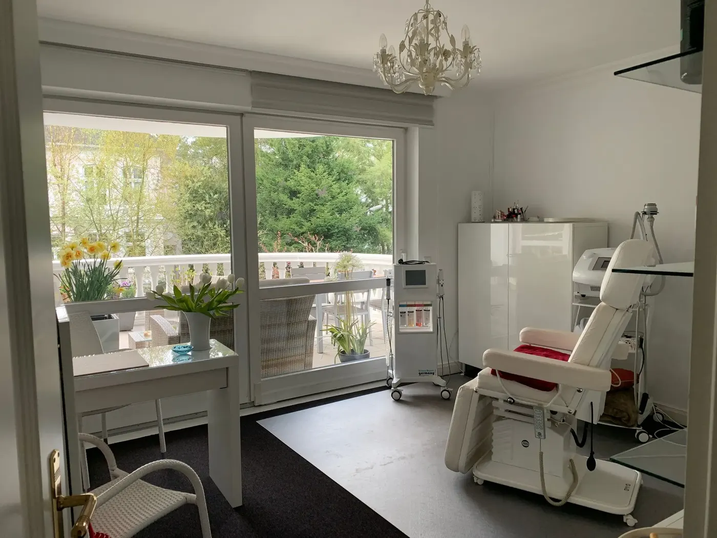 Heller Behandlungsraum mit Behandlungsliege, Geräten und Balkon zum Garten